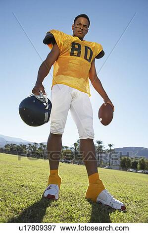 Stock Photo - Football player holding helmet and ball standing on field, low angle, portrait, (portrait). Fotosearch