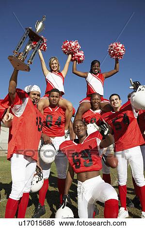 Stock Photograph - Football players and cheerleaders holding up trophy. Fotosearch