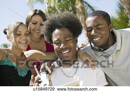 Four friends in back yard looking at video camera screen, front view View Large Photo Image Stock Photo - Four friends in back yard looking at video camera screen, front view. Fotosearch