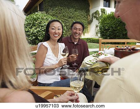 Stock Image - Friends having dinner and drinks in garden. Fotosearch