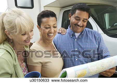 Stock Image - Friends studying road map beside motor home. Fotosearch