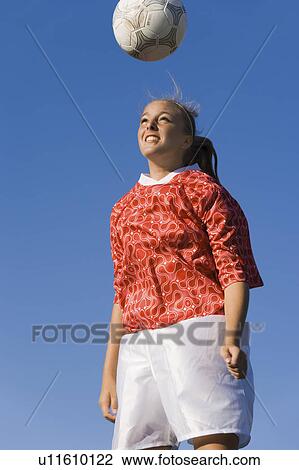 Stock Image - Girl (13-17) heading soccer ball, portrait. Fotosearch