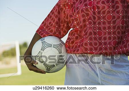 Stock Image - Girl (13-17) holding soccer ball, mid section. Fotosearch