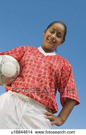 Picture - Girl (13-17) in soccer kit holding ball, portrait, low angle view. Fotosearch