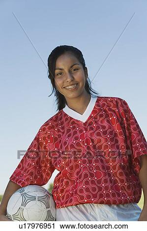 Stock Image - Girl (13-17) in soccer kit holding ball, portrait. Fotosearch