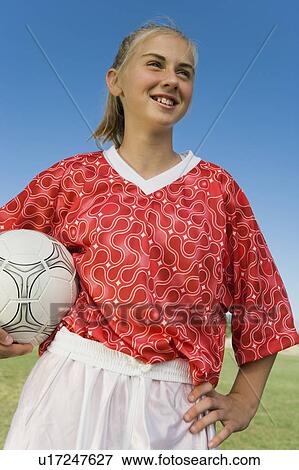 Stock Photo - Girl (13-17) in soccer kit holding ball, portrait, low angle view. Fotosearch