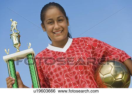 Girl (13-17) in soccer kit holding trophy and ball, portrait View Large Photo Image Stock Photograph - Girl (13-17) in soccer kit holding trophy and ball, portrait. Fotosearch