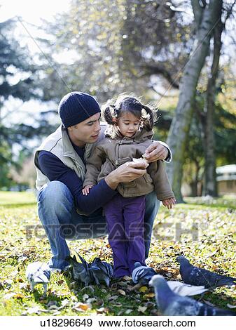 Stock Photo - Girl (3-4) and father feeding pigeons in park. Fotosearch
