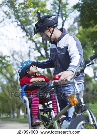 Stock Image - Girl (3-4) and father preparing to ride bicycle in park. Fotosearch