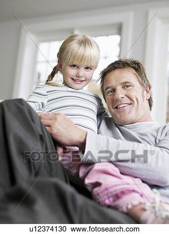 Stock Image - Girl (3-4) sitting in father's lap in house, portrait, low angle view. Fotosearch