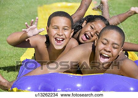 Girl (5-6), boy (7-9), boy (10-12) sliding on water slide, front view portrait. View Large Photo Image Picture - Girl (5-6), boy (7-9), boy (10-12) sliding on water slide, front view portrait.. Fotosearch