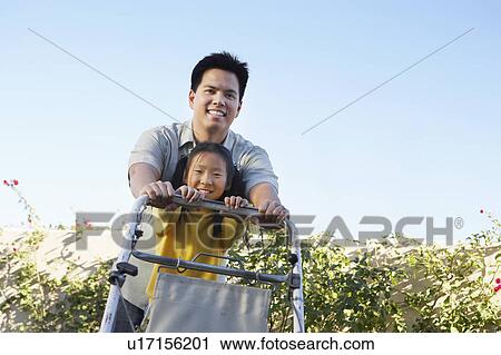 Stock Image - Girl (7-9) helping father mow lawn, portrait, low angle view. Fotosearch