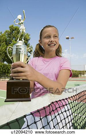Stock Image - Girl at Tennis Net Holding Trophy. Fotosearch
