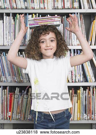 Stock Photo - Girl balancing stack of books on head in library, portrait. Fotosearch