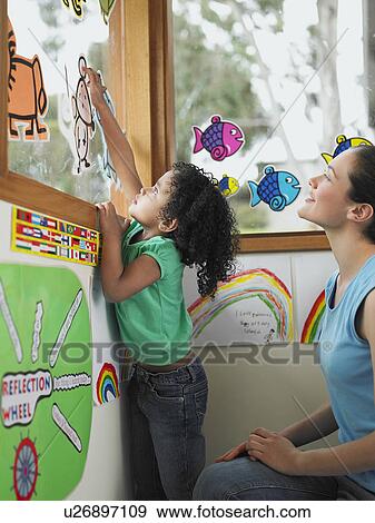 Stock Photo - Girl decorating school window with cut out drawings. Fotosearch