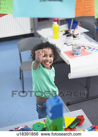 Stock Photograph - Girl pointing up standing in classroom, elevated view. Fotosearch