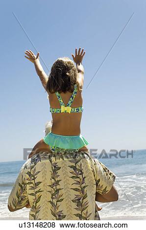 Girl sitting on grandfather's shoulders on beach, arms raised, back view View Large Photo Image Stock Photo - Girl sitting on grandfather's shoulders on beach, arms raised, back view. Fotosearch