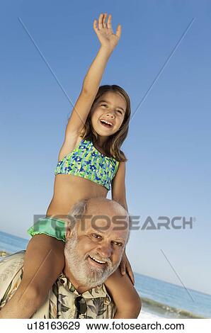 Girl sitting on grandfather's shoulders on beach, arm raised View Large Photo Image Stock Photo - Girl sitting on grandfather's shoulders on beach, arm raised. Fotosearch