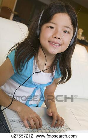 Stock Image - Girl sitting on sofa Using Laptop and Listening to Music, portrait. Fotosearch