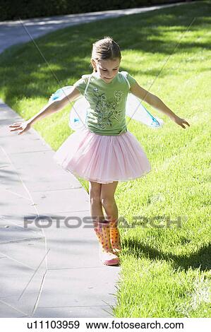 Girl wearing fairy wings and tutu balancing on edge of path, portrait View Large Photo Image Stock Photo - Girl wearing fairy wings and tutu balancing on edge of path, portrait. Fotosearch