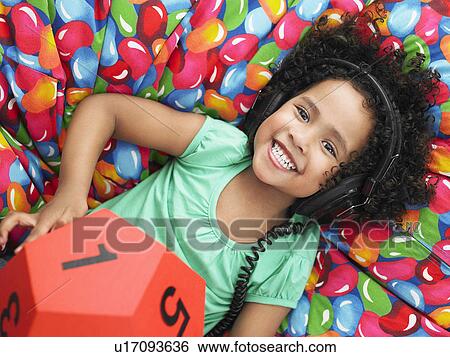 Girl wearing headphones and holding twelve-sided dice reclining on beanbag, view from above, portrait View Large Photo Image Stock Photograph - Girl wearing headphones and holding twelve-sided dice reclining on beanbag, view from above, portrait. Fotosearch