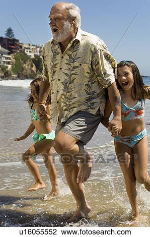 Girls and grandfather running through waves View Large Photo Image Stock Image - Girls and grandfather running through waves. Fotosearch