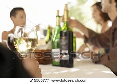 Stock Photo - Glass of white wine on table surrounded by group of people.. Fotosearch