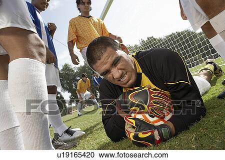 Stock Image - Goalkeeper on ground holding soccer ball, portrait. Fotosearch
