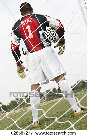 Stock Photo - Goalkeeper standing in goal with ball, back view. Fotosearch