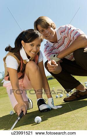 Stock Image - Golfer helping teenage girl line up shot. Fotosearch