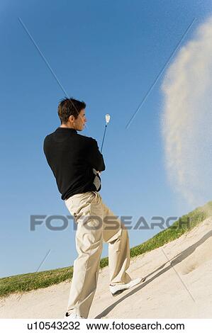 Stock Image - Golfer hitting ball from sand trap. Fotosearch