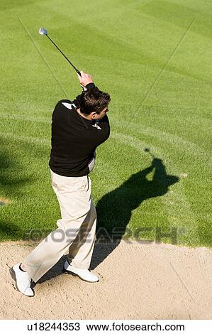 Stock Image - Golfer hitting ball from sand trap, (elevated view). Fotosearch
