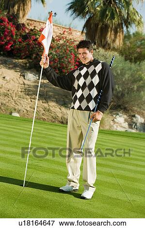Stock Photo - Golfer holding flag in golf cup. Fotosearch