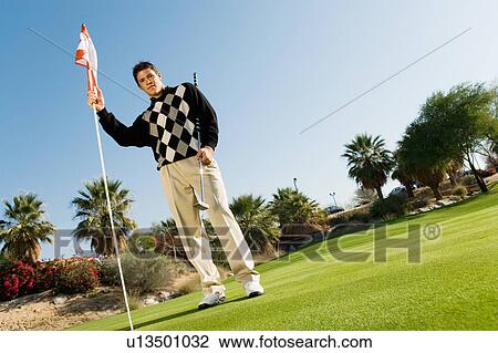 Golfer holding flag on putting green, (low angle view) View Large Photo Image Stock Image - Golfer holding flag on putting green, (low angle view). Fotosearch