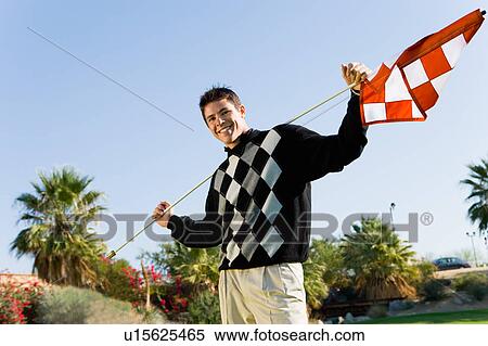 Stock Photography - Golfer holding flagstick on shoulders standing on golf course, (portrait). Fotosearch