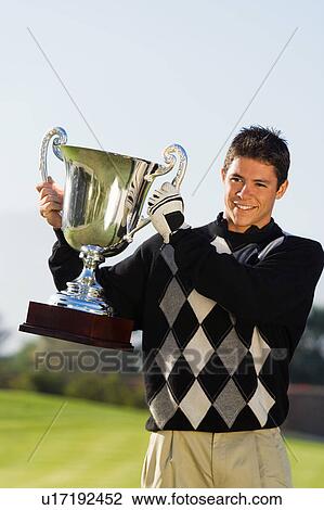 Stock Image - Golfer holding trophy. Fotosearch