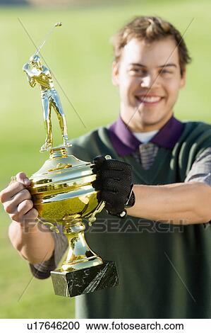 Stock Image - Golfer holding trophy. Fotosearch