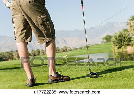 Stock Photography - Golfer standing on golf course holding club, (low section). Fotosearch