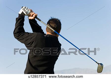 Stock Image - Golfer swinging club, back view. Fotosearch