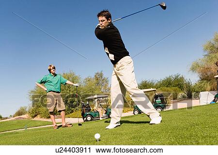 Stock Image - Golfer teeing off next to other player. Fotosearch