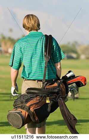 Stock Photograph - Golfer walking through green carrying golf bag, back view. Fotosearch