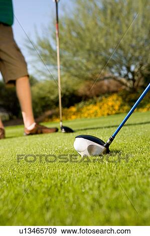 Stock Photo - Golfers holding clubs standing on green, (low section). Fotosearch