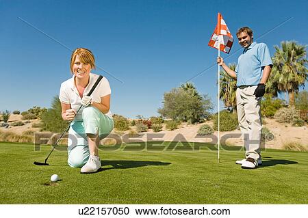 Golfing couple watching ball roll towards golf cup View Large Photo Image Stock Image - Golfing couple watching ball roll towards golf cup. Fotosearch