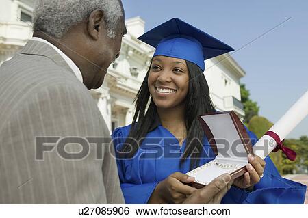 Stock Photograph - Graduate receiving present from father outside university. Fotosearch