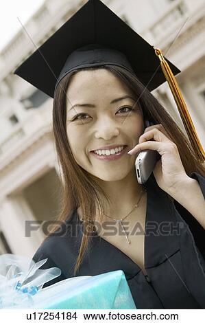 Picture - Graduate with Gift Using Cell Phone. Fotosearch