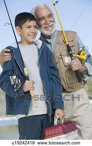 Stock Photo - Grandfather and grandson holding fishing rods outdoors, smiling. Fotosearch