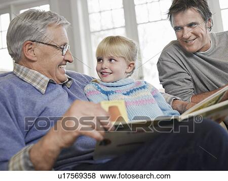Stock Photo - Grandfather reading to girl (3-4), father looking on, in house. Fotosearch