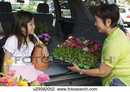Stock Image - Grandmother and granddaughter loading flowers into back of SUV. Fotosearch