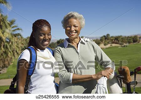 Stock Photography - Grandmother and granddaughter on golf course, smiling, (portrait). Fotosearch