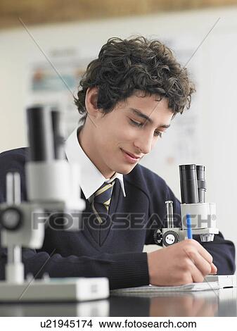 Picture - High school student using microscope and taking notes in classroom. Fotosearch